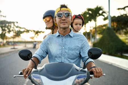 Parents with their little kid riding motorcycle on sunny city streetの写真素材