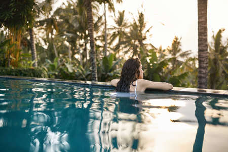 Woman in white swimsuit in outdoor pool on green jungle backgroundの写真素材