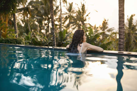 Woman in white swimsuit in outdoor pool on green jungle backgroundの写真素材