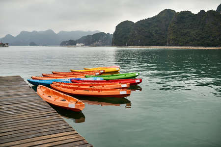 Multicolored canoes moored to wooden pier on nature backgroundの写真素材