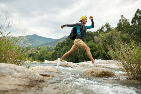 Traveler running through shallow rocky river on nature backgroundの写真素材