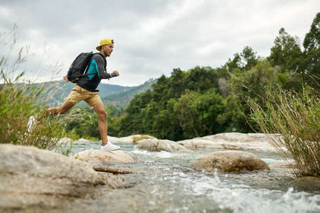 Traveler running through shallow rocky river on nature backgroundの写真素材
