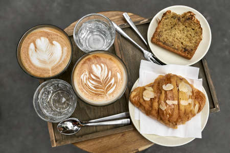 Milk coffee with croissant and bread and water on wooden tableの写真素材