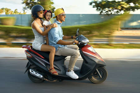Parents with their child riding motorcycle on sunny city streetの写真素材