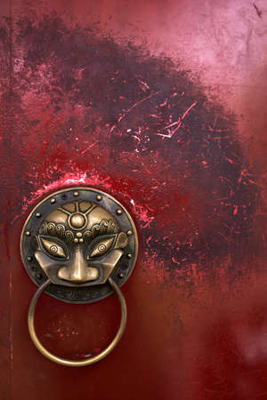 Wonderful asian sculptured bronze handle with a ring on the shabby metal red door. Closeup. Vertical.の写真素材