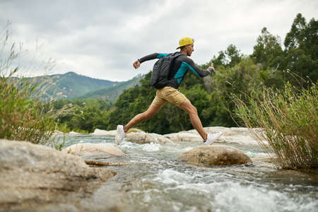 Traveler running through shallow rocky river on nature backgroundの写真素材