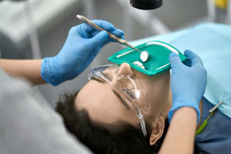 Cute girl in protective glasses and a cheek retractor with a green rubber dam in a dental clinic....