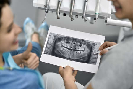 Brunette girl in a patient's bib in a dental clinic. Dentist is showing her a result of an...