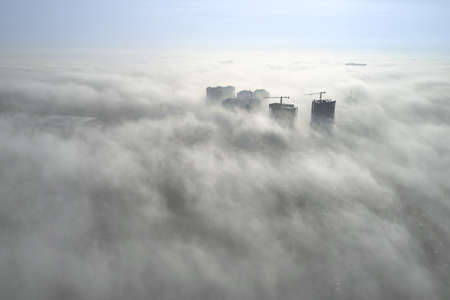 Aerial view at tops of high-rise houses drowning in fogの写真素材