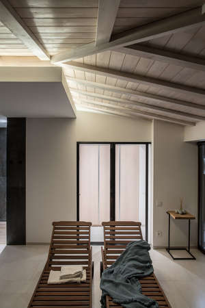 Fancy modern interior with light and dark walls and a wooden ceiling. There are deck chairs with towels and a plaid, stand with aroma sticks and stones, glass doors, luminous lamps. Vertical.の写真素材