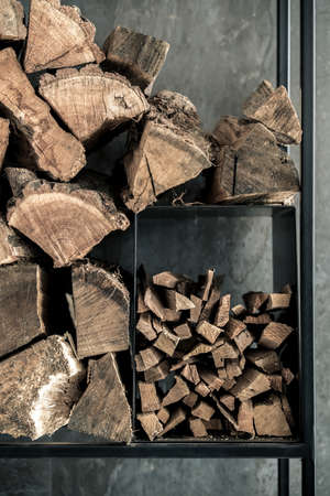 Black stand with firewood on the background of the tiled textured dark wall indoors. Closeup vertical photo.の写真素材