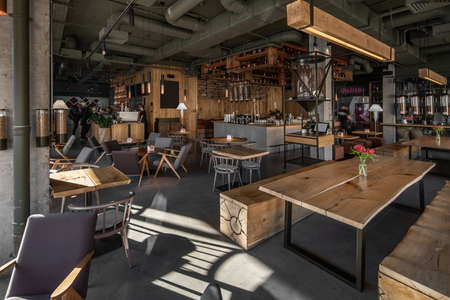 Restaurant in a loft style with textured wooden walls and concrete columns. There are tables with...