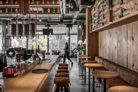 Trendy coffee house in a loft style with textured wooden walls and concrete columns. There are tables with sofas and chairs, shelves with bottles, glass coffee bean dispensers, grain bags, equipment.の写真素材