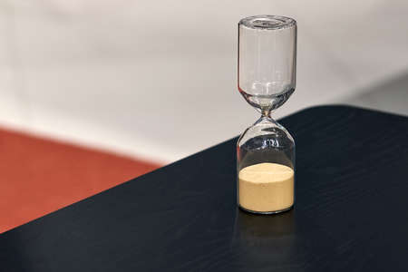Sandglass on the black wooden table on the blurred background in the studio. Closeup photo with...
