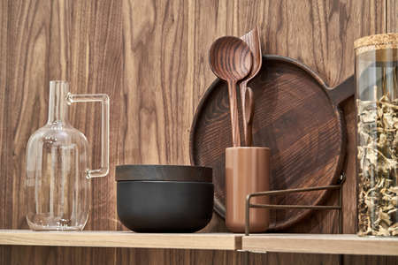 Wooden shelves with wood and ceramic utensil and glass jar and jug on the textured wall background. Closeup horizontal photo.