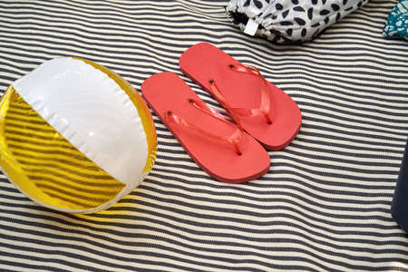 Striped black and white beach mat with a yellow inflatable ball, red rubber slippers and few multicolored drawstring bags. Top view closeup photo. Horizontal.の写真素材