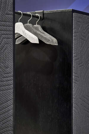Few hangers on the black rack between two dark cabinets on the blue wall background in the illuminated interior. Closeup photo with selective focus. Vertical.の写真素材