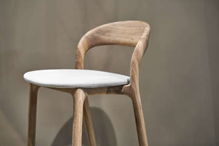 Wooden chair with a soft light seat on the beige wall background in the illuminated interior. Closeup photo with selective focus. Horizontal.の写真素材