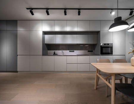 Luminous modern kitchen with light walls and a parquet. There are gray lockers, sink with faucet,...