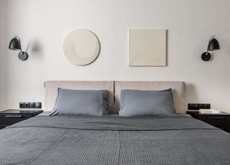 Modern bedroom with white wall with relief pictures. There is a double bed with gray linens and...