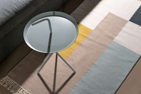 Fancy metal round light stand on the multicolored carpet on the parquet floor in the luminous interior. There is a gray sofa near it. Closeup. Horizontal.の写真素材