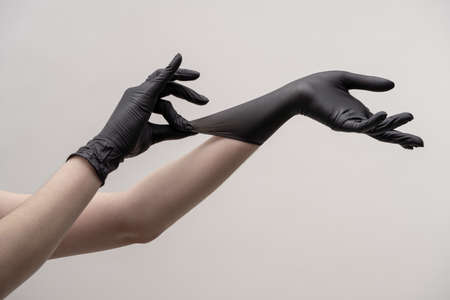Aesthetic female hands in black silicone gloves on a light background. One hand adjusts the glove on the other hand.の写真素材