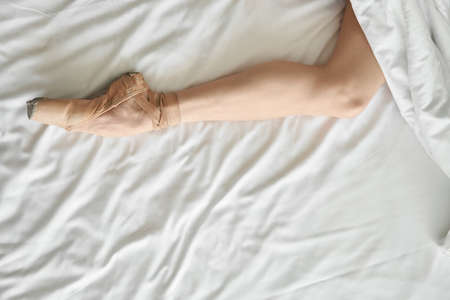 Woman in pointe shoe shows her leg from under coverletの写真素材