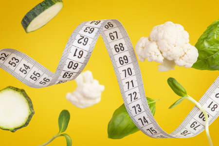 White measuring tape with pieces of vegetables and herbs on a yellow backgroundの写真素材