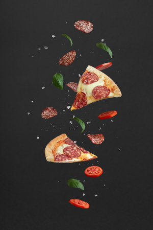 flying pieces of pizza and ingredients on a black backgroundの写真素材