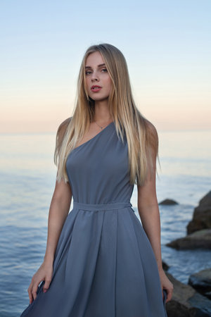 Beautiful girl blonde in a long gray dress on the background of the seaの写真素材