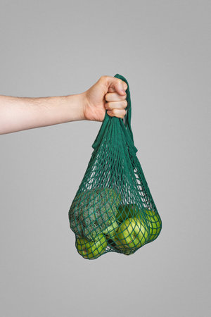 zero waste packaging.A shopping bag with green apples in a man's hand on a gray backgroundの写真素材