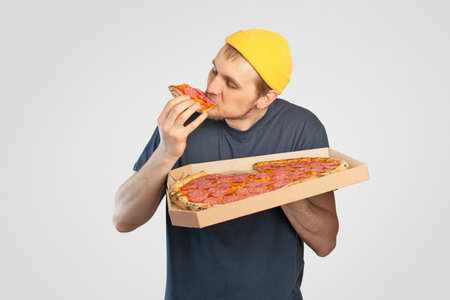 Young man eating pizza with a box in his handsの写真素材