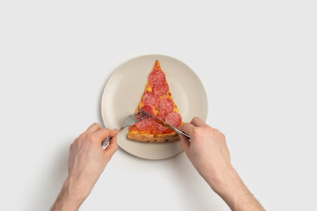 Male hands with a slice of pizza in a gray plate on a white background with a knife and forkの写真素材