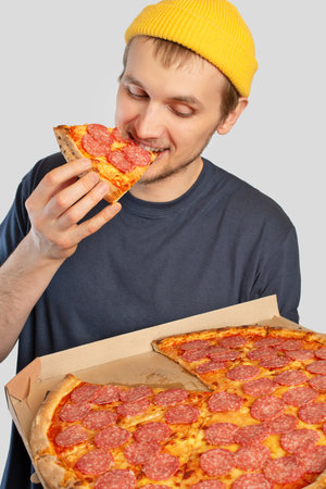 Young man eating pizza with a box in his handsの写真素材