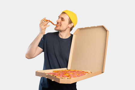 Young man eating pizza with a box in his handsの写真素材
