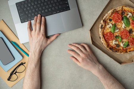 A man works and eats pizza, top view, hands on the desktop. Pizza delivery.の写真素材