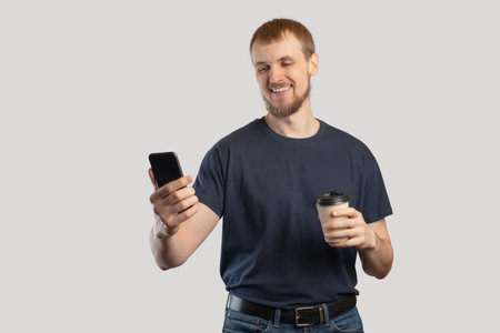 Smartphone in male hands close-upA European man with a phone and coffee in his hands on a gray isolated backgroundの写真素材