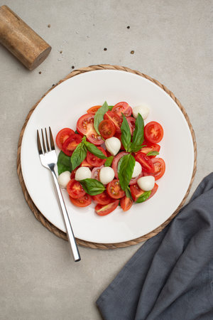Salad with cherry tomatoes and mozzarella in a white plate on a gray backgroundの写真素材