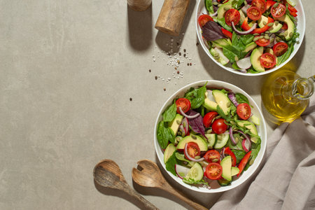 Fresh green salad with tomatoes, cucumbers, radish, sweet pepper and avocado in a white plate on a gray background.の写真素材