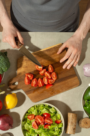 A man in a gray kitchen apron prepares a salad, close-upの写真素材