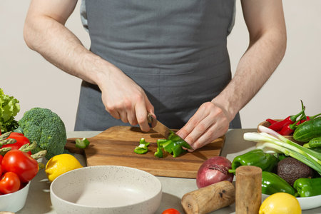 A man in a gray kitchen apron prepares a salad, close-upの写真素材