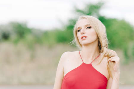 young girl with white hair on nature on a green background in a red dress without photoshopの写真素材