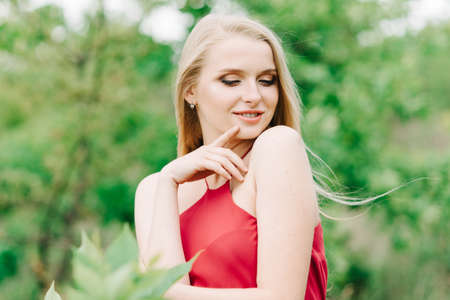 young girl with white hair on nature on a green background in a red dress without photoshopの写真素材