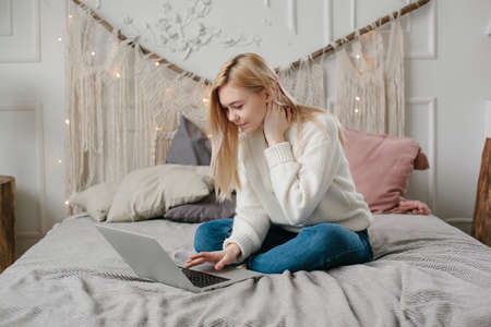 Girl student study online with teacher, happy young woman look at laptop sit on bed at home.の写真素材