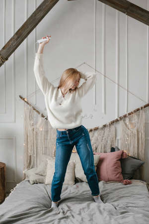 Happy young woman in headphones listening to music from smartphone and dancing on bed at home.の写真素材