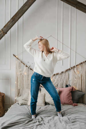 Happy young woman in headphones listening to music from smartphone and dancing on bed at home.の写真素材
