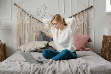 Girl student study online with teacher, happy young woman look at laptop sit on bed at home.の写真素材