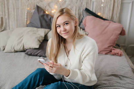 young caucasian woman sits on bed and uses a smartphoneの写真素材