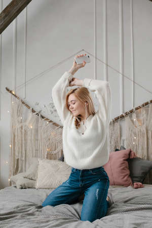 Happy young woman in headphones listening to music from smartphone and dancing on bed at home.の写真素材