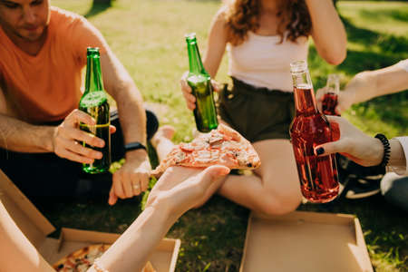 Friends drink beer and alcohol and eat pizza outdoors, hands close-upの写真素材